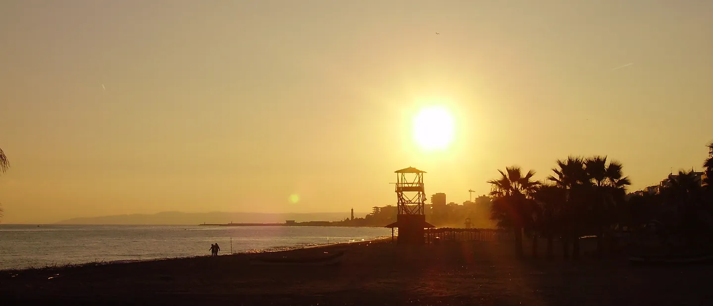 Atardecer en el paseo marítimo de Estepona, con la torre del socorrista, palmeras y el faro a lo lejos